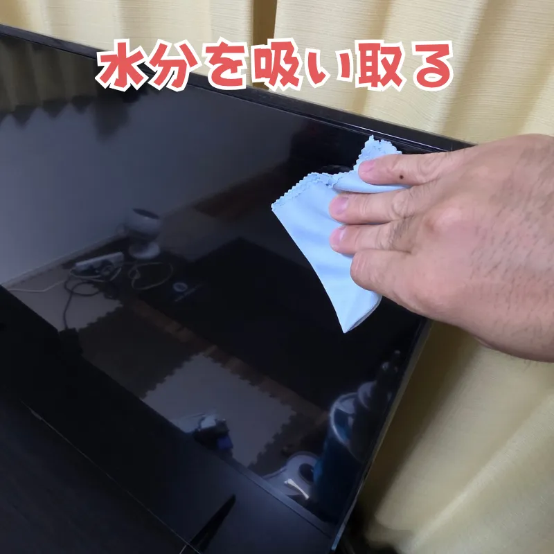 乾いたマイクロファイバークロスでテレビ画面の水分を優しく吸い取っている様子。