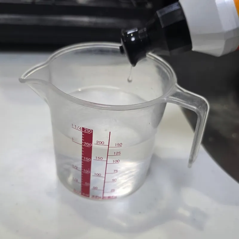 計量カップに入れた200mlのぬるま湯に中性洗剤を垂らしている様子。