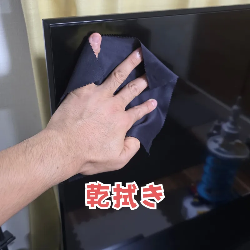 黒いマイクロファイバークロスでテレビ画面を乾拭きしている様子。