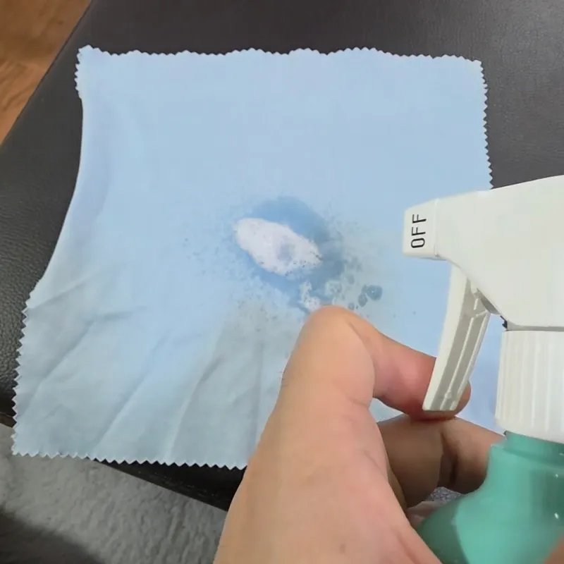 合皮に直接吹きかけず、広げたクロスにクリーナーをスプレーしている様子。