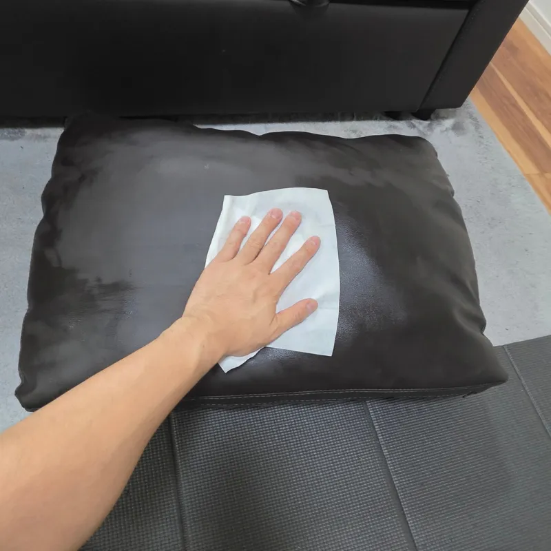 ソファーの背もたれクッションに専用の白いシートを当てて、表面を優しく拭き取っている様子。