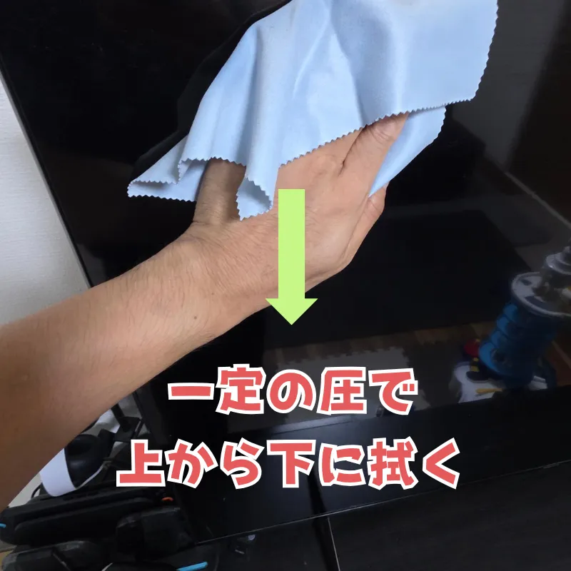 マイクロファイバークロスを使い、一定の力で上から下へ向かってテレビ画面を拭き上げる様子。