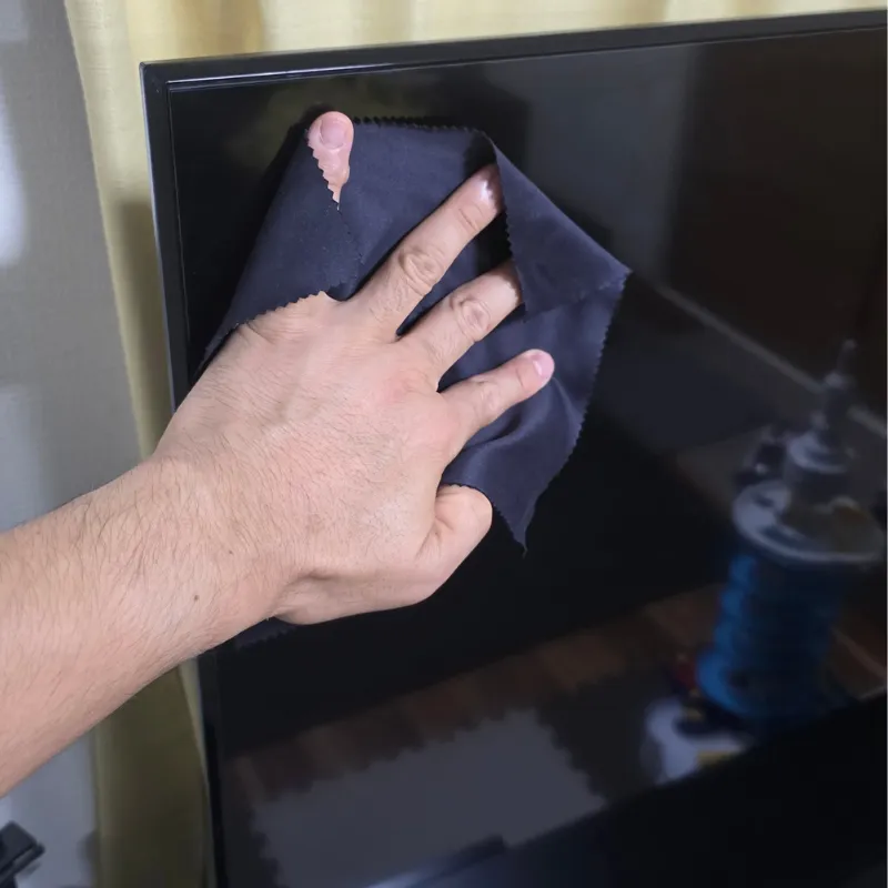 黒いマイクロファイバークロスでテレビの画面を拭いている様子。