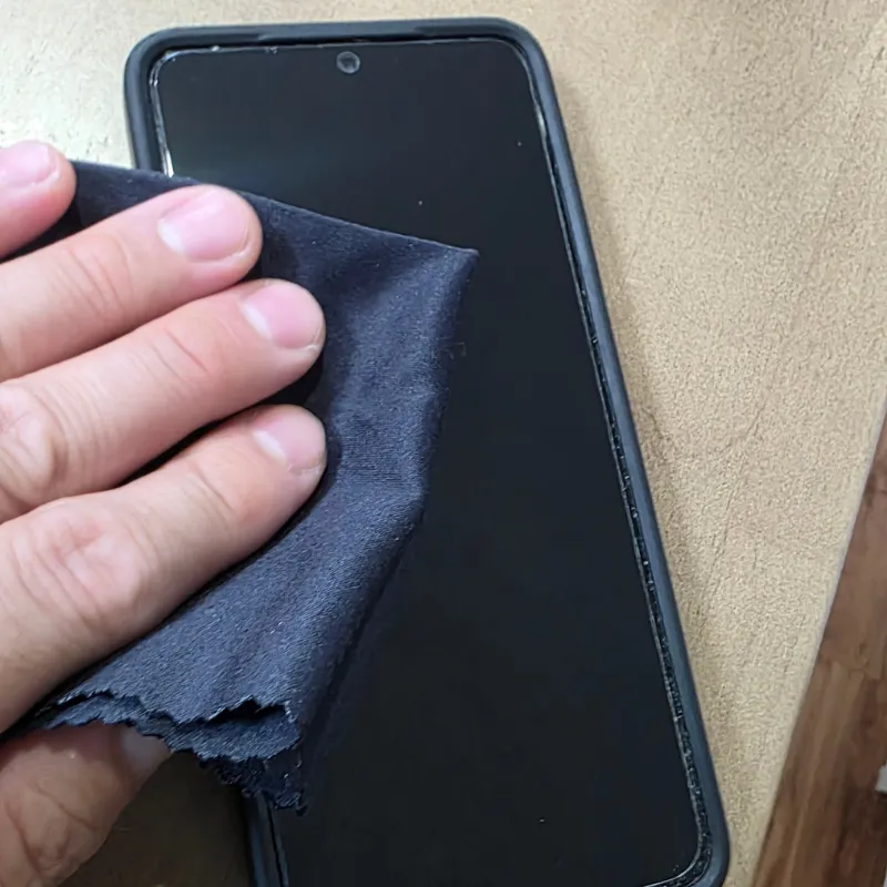 スマートフォンの画面の端を、黒いマイクロファイバークロスでお掃除をしている。