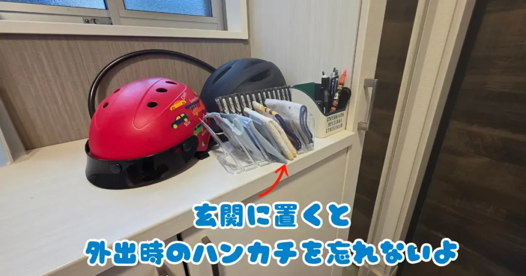 玄関の棚の上に、子供用のヘルメットやペン立てと並んで、ハンカチが収納された透明なスタンドが置かれている様子。