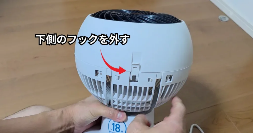 後面カバーの下部にある固定フックを手で外している様子。