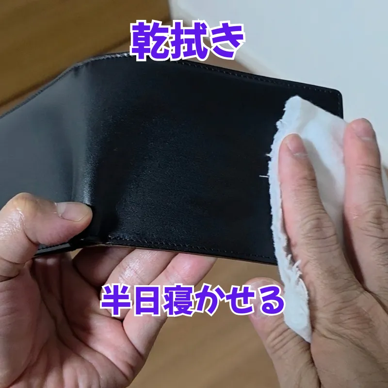 15分放置した後、乾拭き用の綺麗なクロスを使って、表面の余分なミンクオイルを優しく拭き取っている黒い革財布。