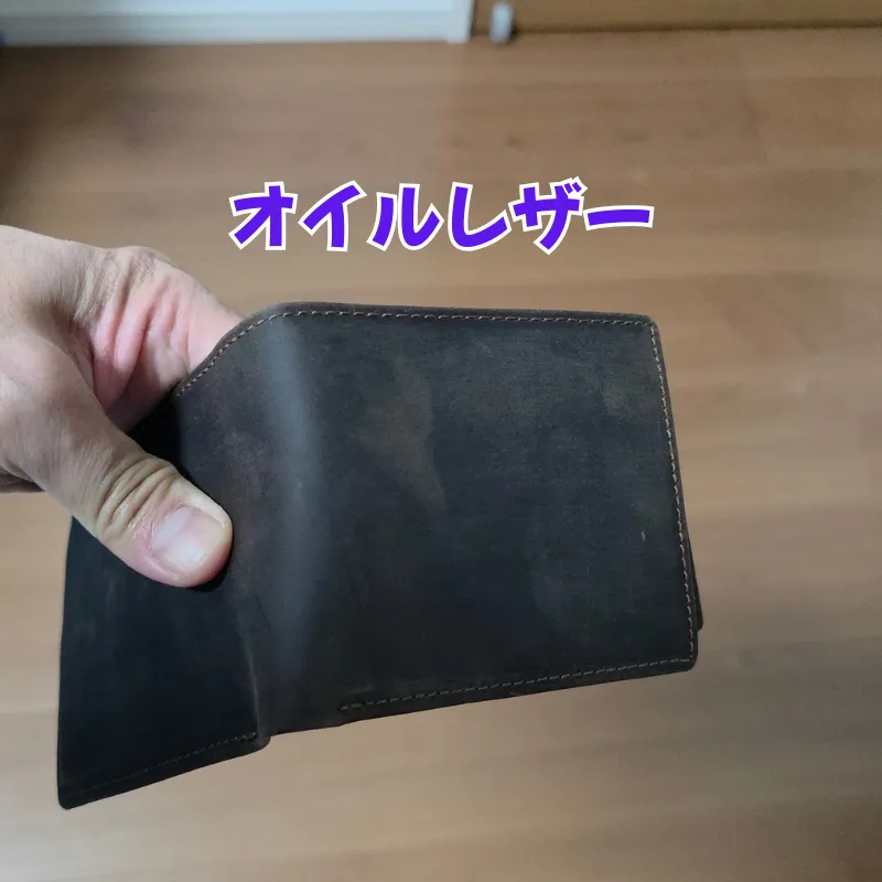 手で持たれたオイルレザー（クレイジーホースレザー）の財布。独特のマットな質感や色ムラが確認できる。