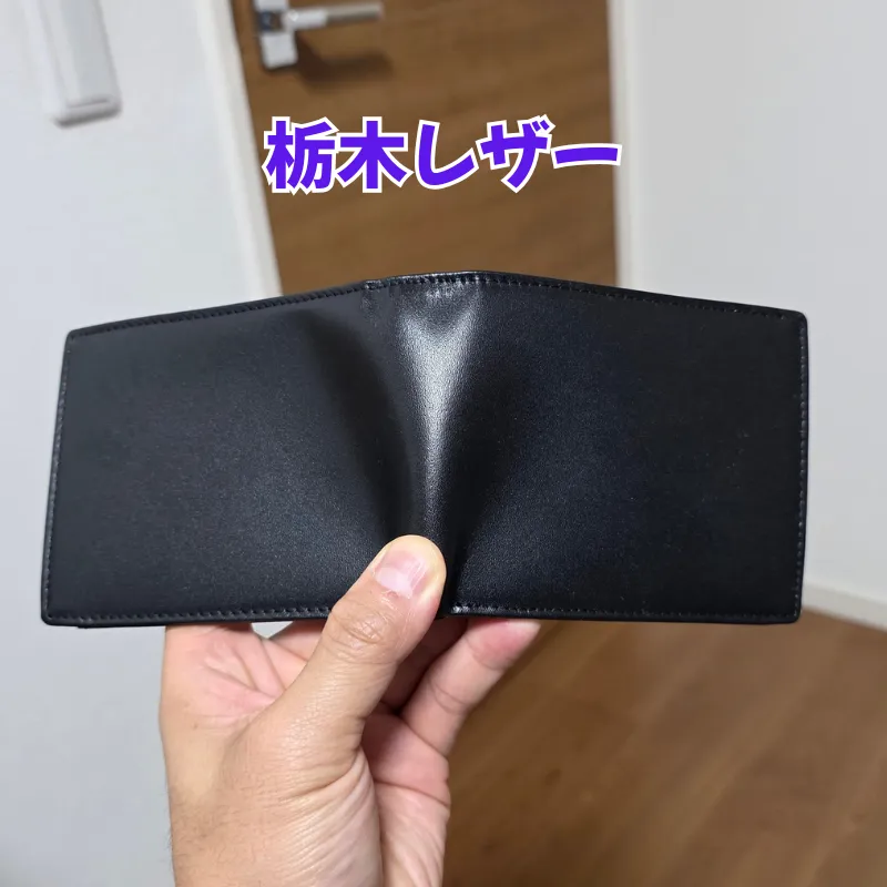ミンクオイルの塗りすぎによる型崩れのリスクを説明するために用いられている、手で持たれた薄手の黒い栃木レザーの財布。