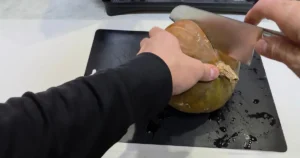黒いまな板の上で、丸ごとのカボチャに包丁で刃を入れている様子。