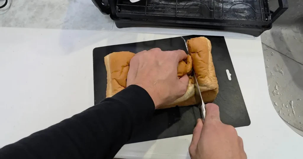 黒いまな板の上で、食パンを包丁で切っている様子。