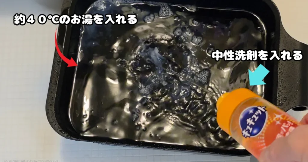 黒い桶に溜めた約40度のお湯の中に、プラスチックの油汚れを落とすための中性洗剤を注ぎ入れている様子。