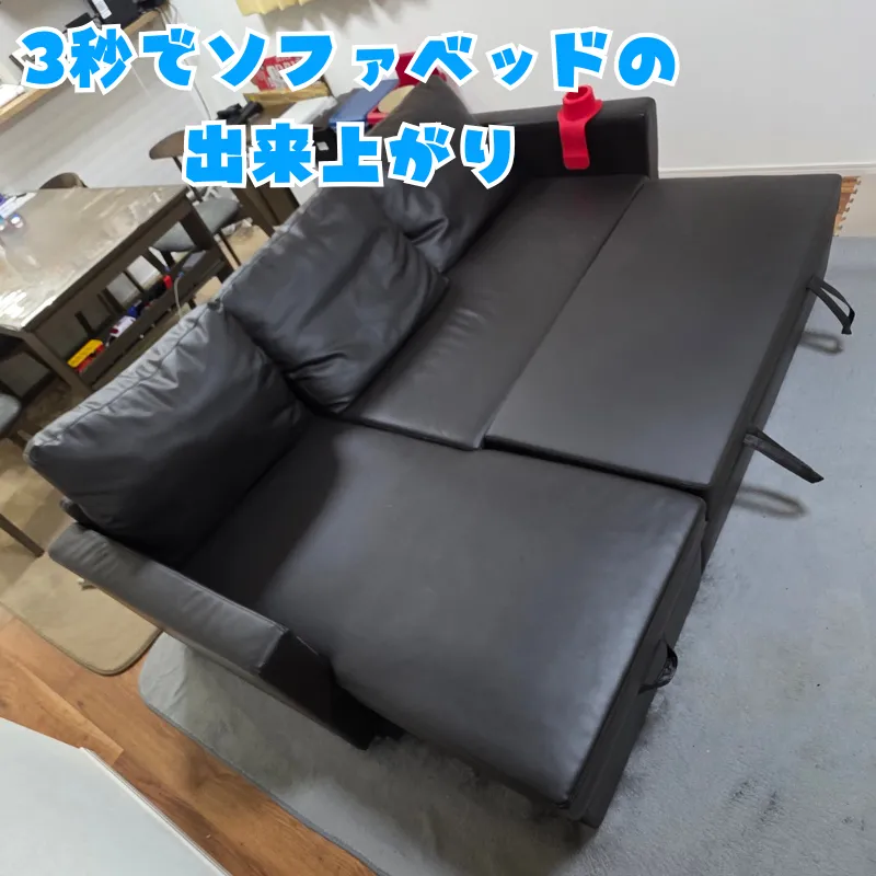 黒いカウチソファの座面下から引き出し部分を展開し、広大なベッドスペースが完成した状態。