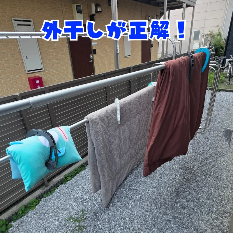 クッションや毛布、掛け布団などの寝具が屋外の物干し竿に干されている様子。