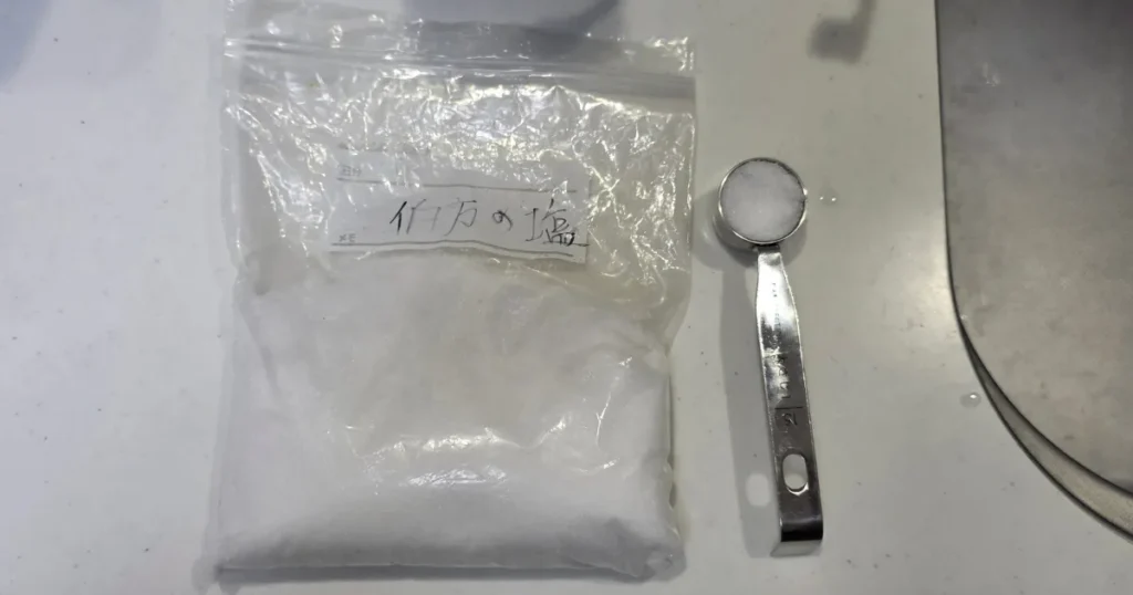 塩が入った袋の横に、塩をすりきり一杯入れた計量スプーンが置かれている。