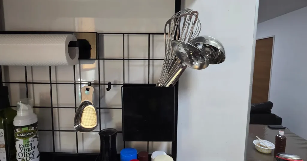 山崎実業(tower)のレンジフードメッシュパネルに取り付けられたツールホルダーに、泡立て器やお玉などのキッチンツールが収納されている様子。