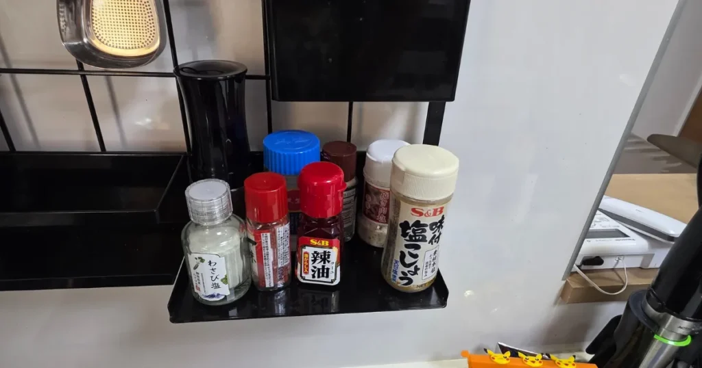 山崎実業(tower)のレンジフードメッシュパネルに取り付けられた調味料ラックに、塩こしょうや辣油などの小瓶が並んでいる様子。