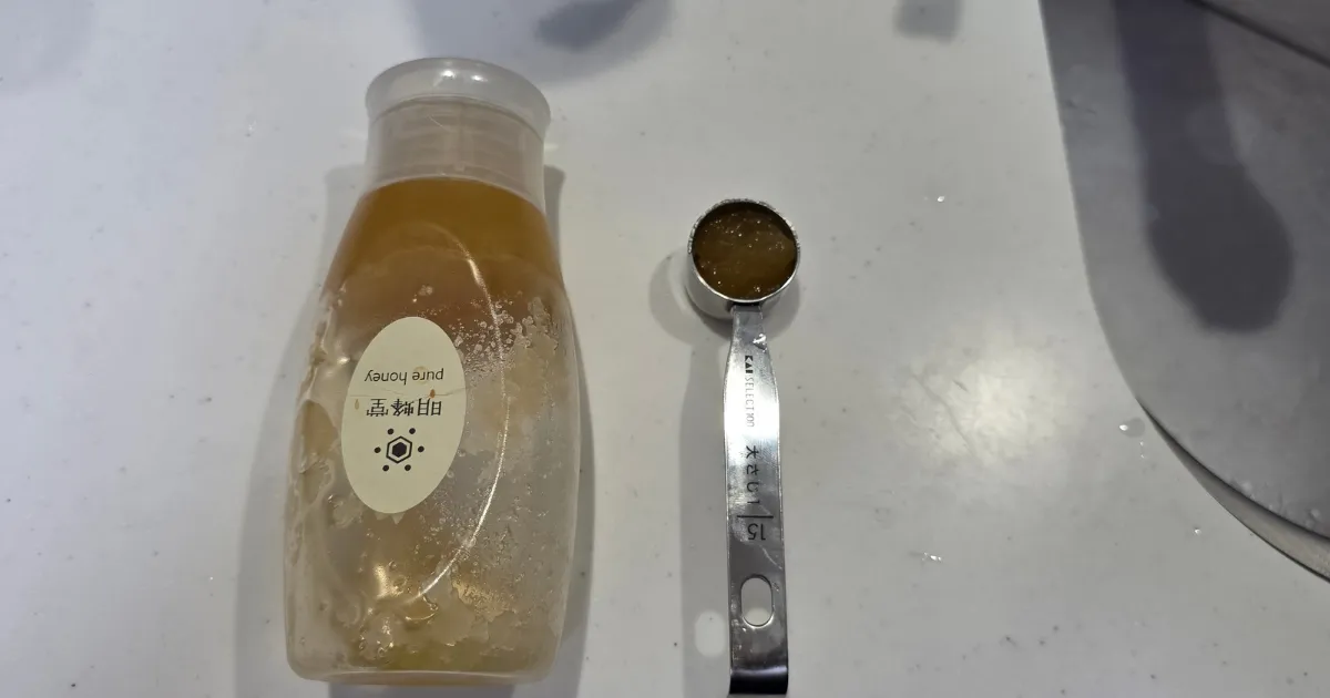 蜂蜜のボトルの横に、はちみつを入れた計量スプーンが置かれている。