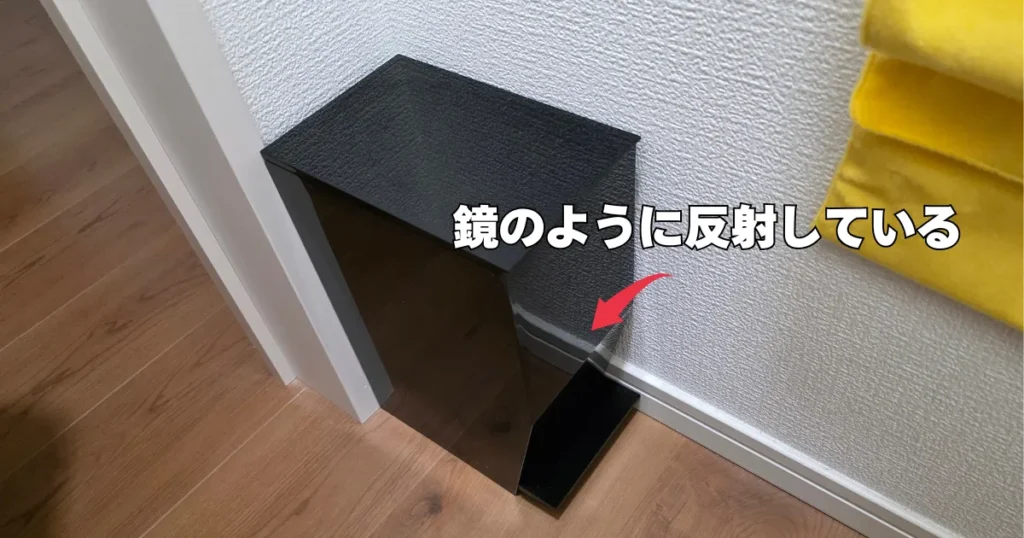 表面が鏡のように壁を反射している、黒いtowerのサニタリーボックス。