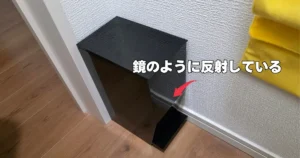 表面が鏡のように壁を反射している、黒いtowerのサニタリーボックス。