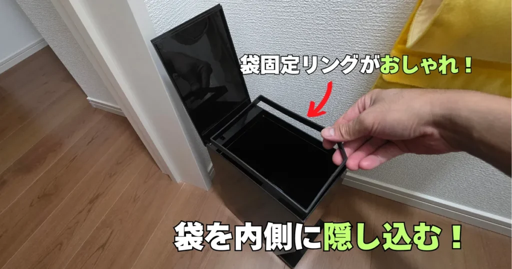 黒いtowerのサニタリーボックスのフタを開け、ゴミ袋を内側に隠すための袋固定リングを手で持ち上げている様子。