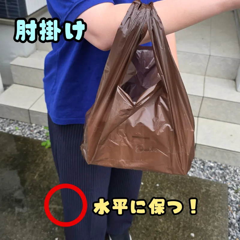 ケーキ箱が入ったレジ袋の持ち手を腕に通し、肘にかけて水平に保つ推奨される持ち方。
