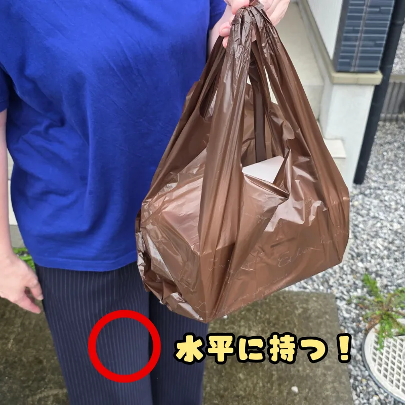 ケーキ箱が入ったレジ袋の持ち手を片手で握り、腕を下げて持つ推奨される持ち方。