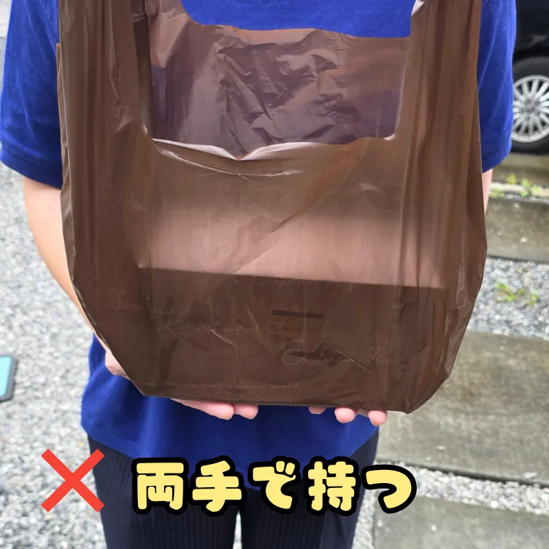 ケーキ箱を両手で下から支えて持つ、推奨されない持ち方。