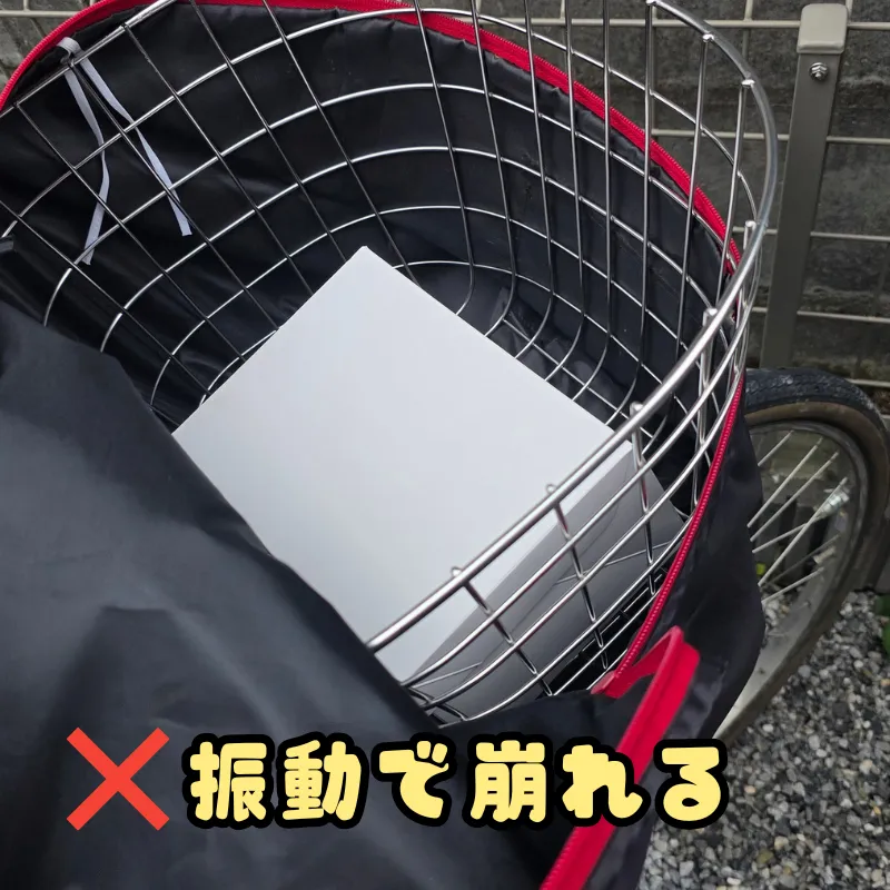 自転車の前カゴに入れられ、斜めに傾いて隙間ができている白いケーキ箱。