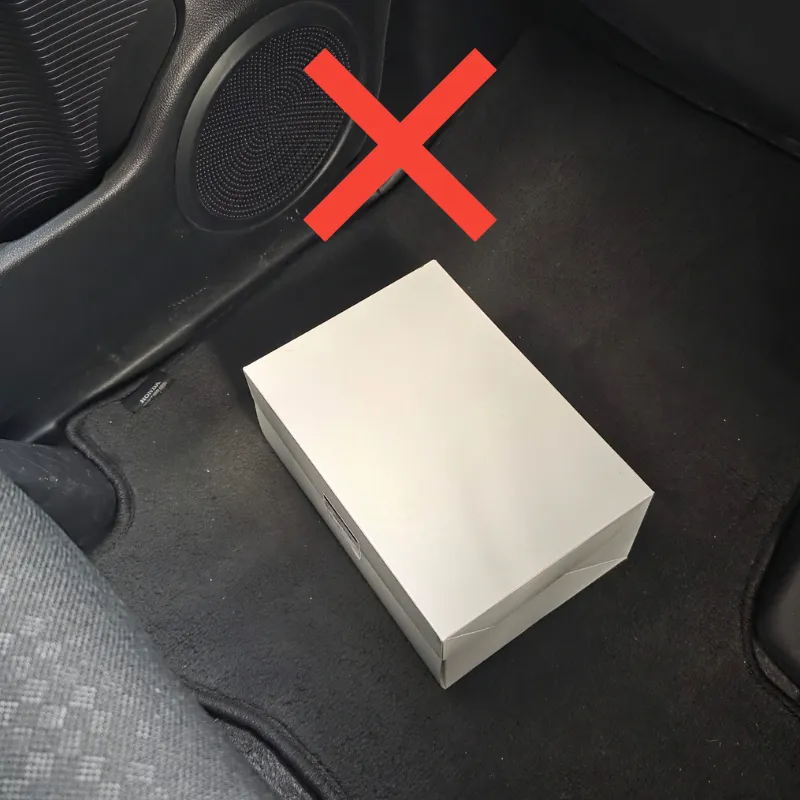 車の助手席の足元にあるフロアマットに直接置かれた白いケーキ箱。