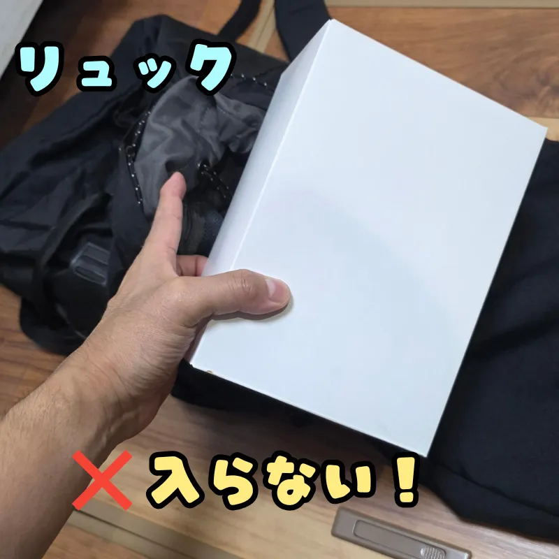 黒いリュックサックの上に重ねられ、サイズが大きすぎて中に入らないことがわかる白いケーキ箱。
