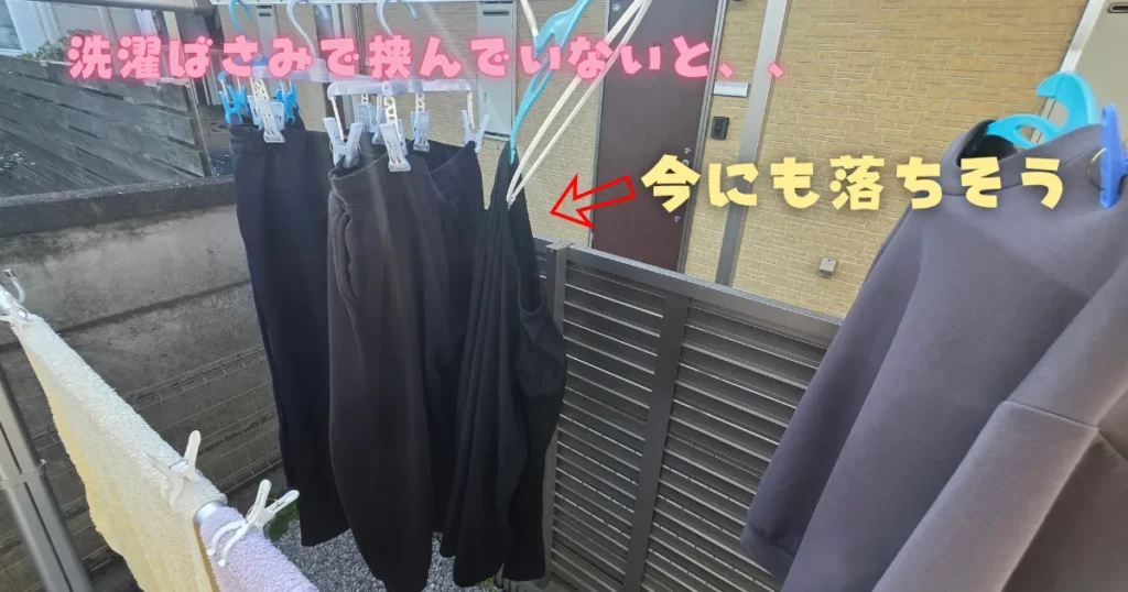 外干しの物干し竿に掛けられたピンチハンガーに、洗濯バサミを使わずに干した黒い衣類が、ハンガーからずり落ちて今にも地面に落下しそうな状態になっている様子。