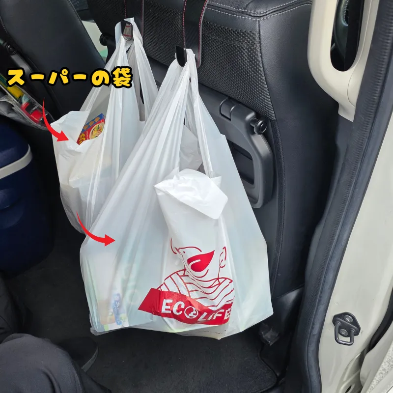 車のシートフックに掛けられた、スーパーでまとめ買いした荷物が入ったレジ袋。