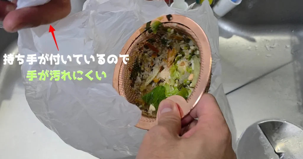 銅製のゴミ受けに溜まった生ゴミを捨てる際、レジ袋の取っ手部分を掴んで袋の口を広げている様子。