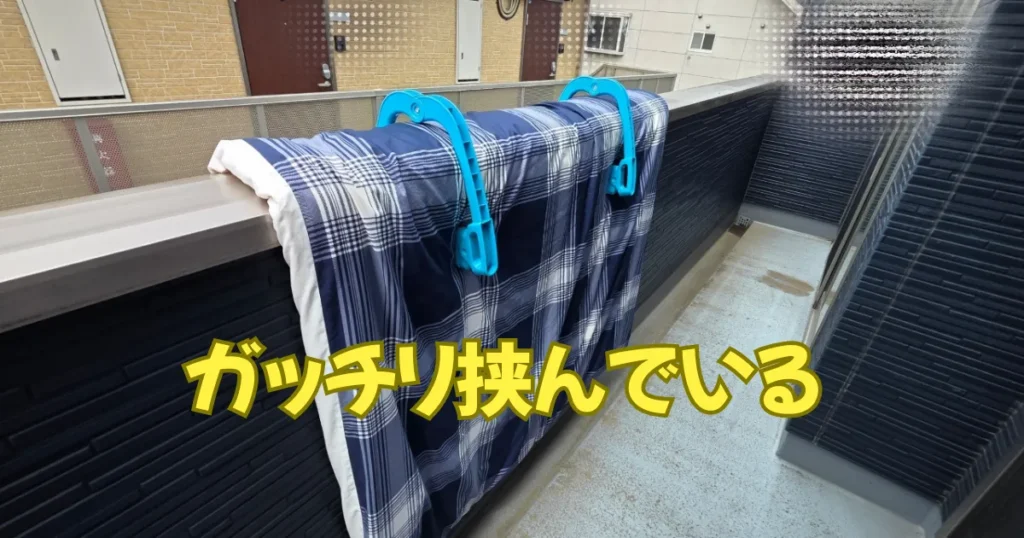 マンションの太い手すりに対し、超特大サイズの布団バサミ2個を使って布団を干している。