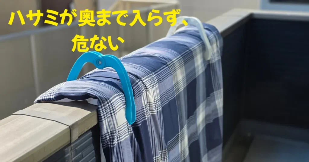 マンションの太い手すりに標準サイズの布団バサミを使った結果、幅の限界で奥まで挟み込むことができず、布団を安全に固定できていない危険な状態。