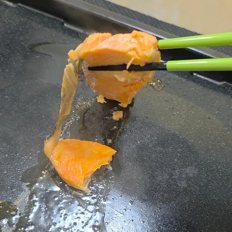 角皿に直接置いて焼いた鮭を箸で持ち上げると、身が割れて皮が剥がれている状態。