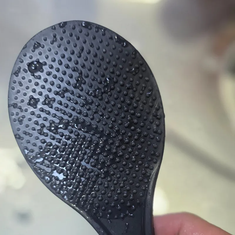 水滴が多数付着した状態の、凹凸加工のある黒いしゃもじの表面。