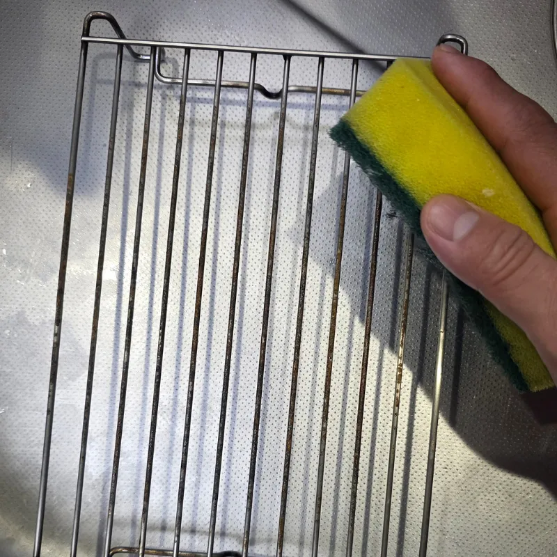 緑色のハードたわしで、サビた網を擦って掃除する様子。