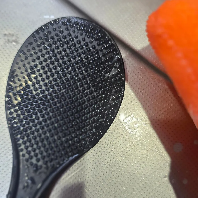 ご飯粒がこびりついた凹凸加工のある黒いしゃもじの表面。