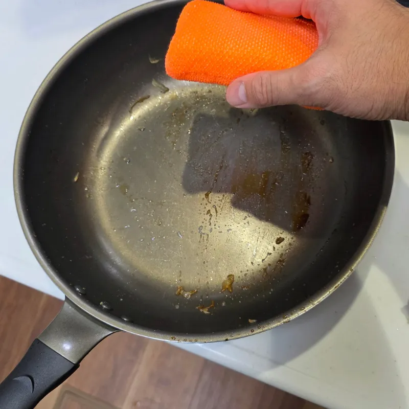 キッチンシンク内に置かれた、少量の水滴と油汚れが付着した状態の使用後のフライパン。