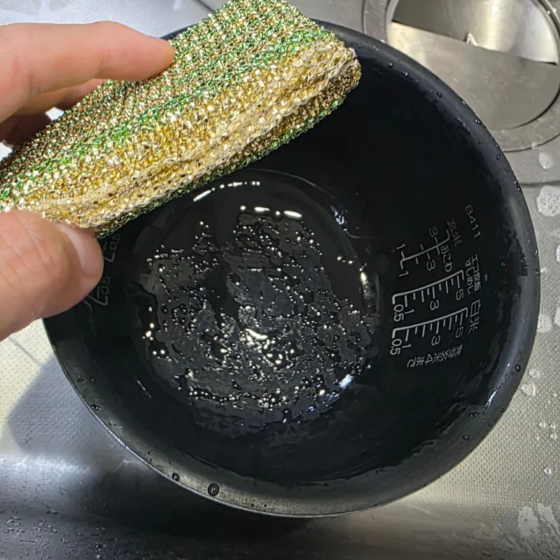 炊飯器の内釜のこびりついたご飯粒を、アルミ蒸着ネットで洗う様子。